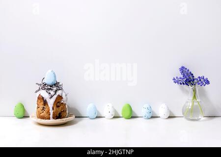 Homemade traditionla Easter kulich cake with chocolate nest and eggs on plate standing on white marble table with colored eggs in row. Traditional ort Stock Photo