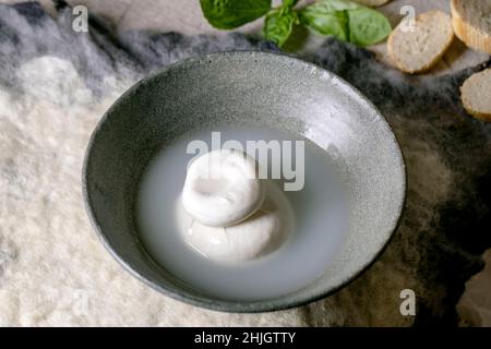 Traditional italian burrata knotted cheese in grey ceramic bowl on table. Bread, olives, greens around. Ingredients for healthy mediterranean dinner. Stock Photo