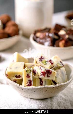 Variety of homemade toffee chocolate almond nuts candy, dark chocolate truffle, white chocolate candy bar in bowls on white linen table cloth. Handmad Stock Photo