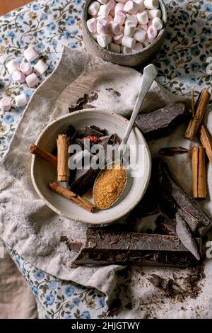 Ingredients for make hot chocolate winter drink in bowl. Chopped dark chocolate, species, cane sugar, marshmallows on rustic linen tablecloth in count Stock Photo