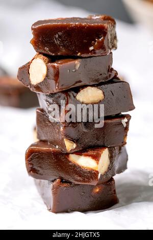 Stack of homemade toffee salted caramel chocolate almond nuts candy on crumpled paper over white linen tablecloth. Handmade food sweet gifts for any h Stock Photo