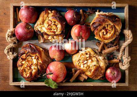 Sweet apple sticky cinnamon rolls buns with gardening apples and cinnamon sticks in wooden colorful tray. Traditional home bakery. Flat lay Stock Photo