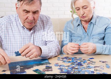 Elderly couple collecting puzzles at home, old couple play jigsaw Stock Photo