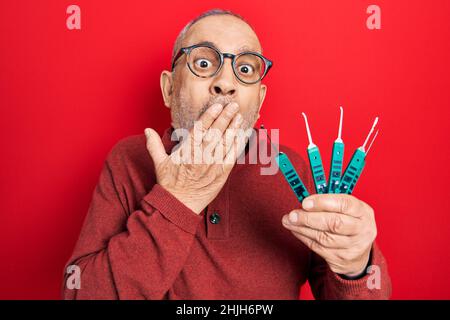 Handsome mature man holding picklock to unlock security door covering mouth with hand, shocked and afraid for mistake. surprised expression Stock Photo