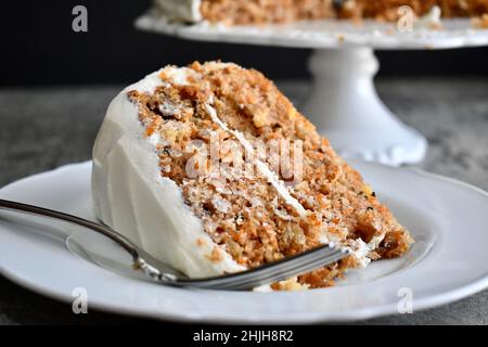 Slice of carrot cake with cream cheese frosting on a white plate with fork Stock Photo