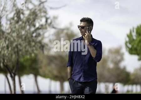 Young middle-aged male walking alone and using the smart phone along the Lisbon riverside Stock Photo