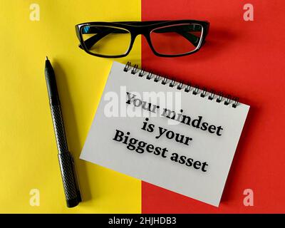 Motivational and inspirational concept - Your mindset is your biggest asset. With glasses, pen, yellow and red background. Motivational concept. Stock Photo