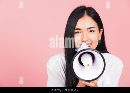 Portrait of happy Asian beautiful young woman teen confident smiling face holding making announcement message shouting screaming in megaphone, studio Stock Photo