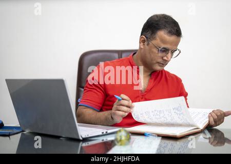 An Indian man in glasses with laptop computer working at an office Stock Photo