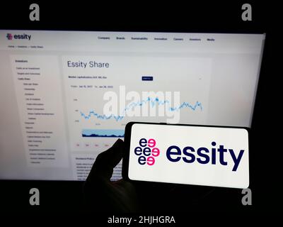 Person holding mobile phone with logo of Swedish consumer goods company Essity AB on screen in front of business webpage. Focus on phone display. Stock Photo