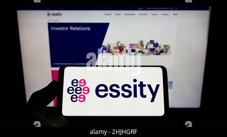 Person holding smartphone with logo of Swedish consumer goods company Essity AB on screen in front of website. Focus on phone display. Stock Photo