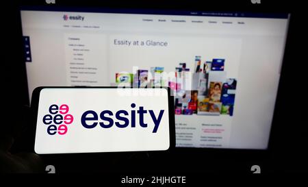 Person holding cellphone with logo of Swedish consumer goods company Essity AB on screen in front of business webpage. Focus on phone display. Stock Photo