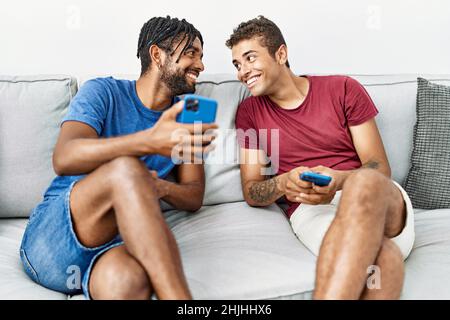 Two men friends using smartphone sitting on sofa at home Stock Photo