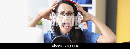 Young woman shouts in headphones in front of microphone Stock Photo
