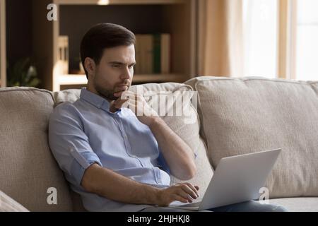 Thoughtful young man working on computer at home. Stock Photo