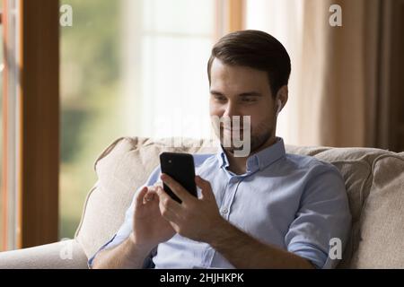 Happy young man in earbuds using cellphone. Stock Photo