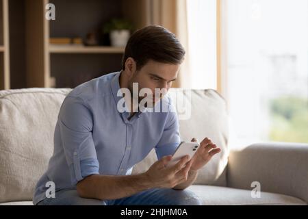 Concentrated young man using smartphone at home. Stock Photo