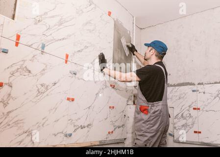 Handyman instaling ceramic tiles on the bathroom wall Stock Photo