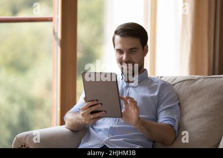 Joyful millennial man using digital computer tablet. Stock Photo