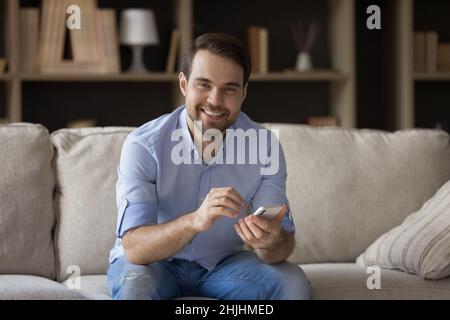 Portrait of smiling relaxed young man using cellphone at home. Stock Photo