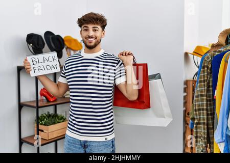 Young arab man customer holding shopping bags and black friday banner at clothing store Stock Photo