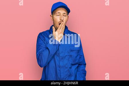 Bald man with beard wearing builder jumpsuit uniform bored yawning tired covering mouth with hand. restless and sleepiness. Stock Photo