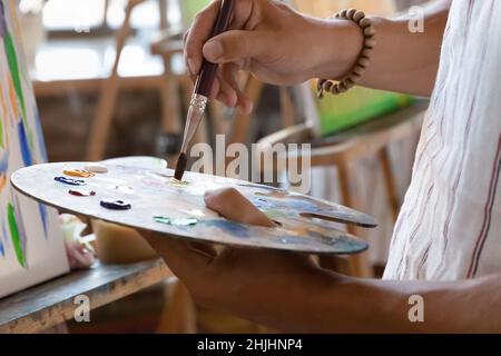 Artist hand holding palette at easel with oil, acrylic paints Stock Photo
