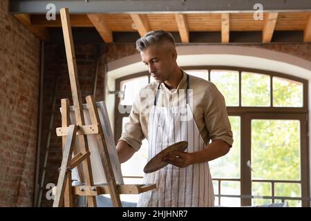 Serious professional artist man in craft apron working in studio Stock Photo