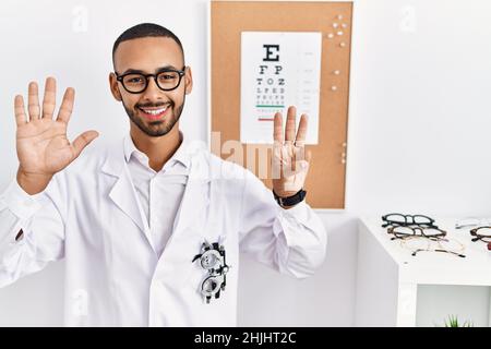 African american optician man standing by eyesight test showing and pointing up with fingers number eight while smiling confident and happy. Stock Photo