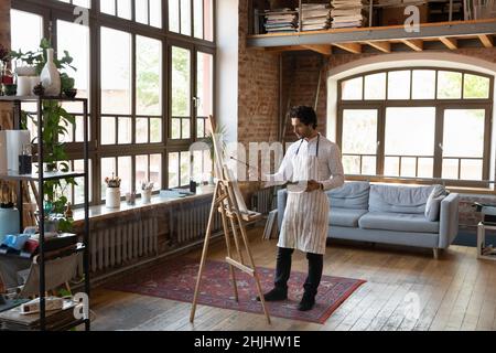 Young male artist working in home studio, standing at easel Stock Photo