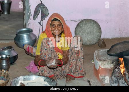 Grandmother making and cooking fresh food in a rural village in a vintage kitchen using firewood in earthen chulhas. smile on face. Stock Photo