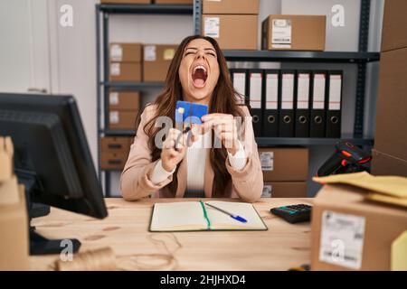 Young brunette woman working at small business ecommerce cutting credit card angry and mad screaming frustrated and furious, shouting with anger looki Stock Photo