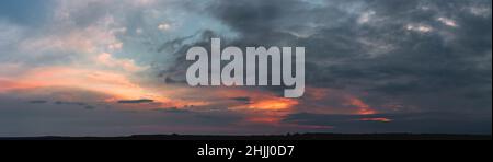 Dramatic gloomy panorama of bright saturated sunset with large dark clouds Stock Photo