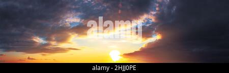 Panorama of dramatic colorful sunset with dark and bright clouds. The sun's rays are breaking through the cloudy sky. Dark clouds against a bright sat Stock Photo
