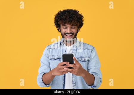 Happy indian young man using cell phone isolated on yellow background. Stock Photo
