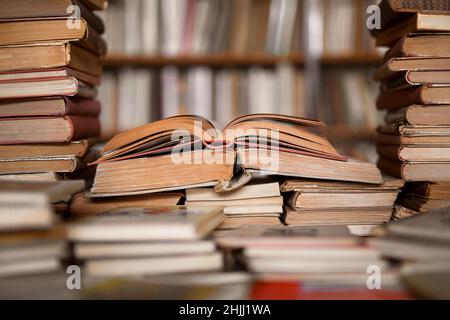 Old books on the table in the antiquarian bookshop - opened books, book pages, blurred bookshelf in the background Stock Photo