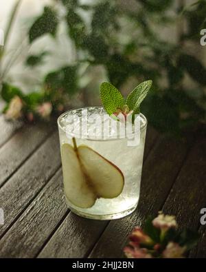summer cocktail decorated with mint, lemon and slices pears on a wooden table on a floral background Stock Photo