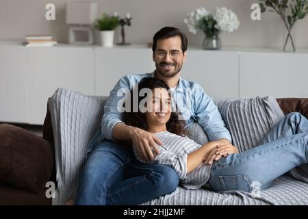 Couple relaxing on sofa hugging posing looking at camera Stock Photo