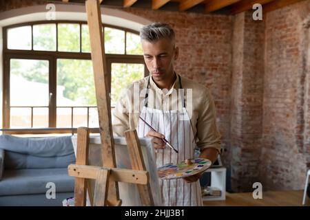 Pensive inspired handsome artist man drawing in paints Stock Photo