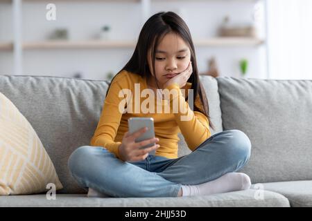 Bored teenager japanese girl using mobile phone at home Stock Photo