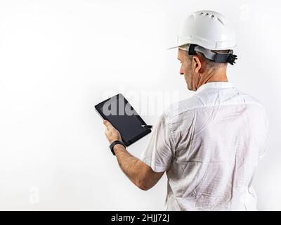Male engineer in a white hard helmet. Middle-aged man in a white shirt with a tablet computer. Back view. Isolated portrait on a white background. Mal Stock Photo
