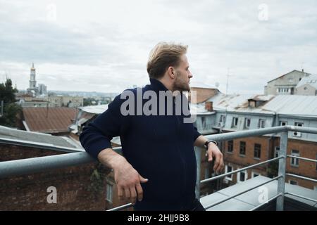 handsome white blond man stands on the roof and looks at the city, professional, break at work Stock Photo