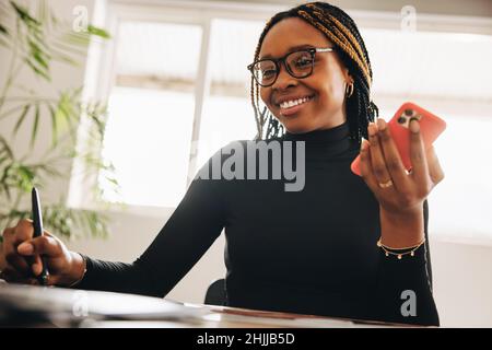 Smiling graphic designer taking a phone call in her home office. Creative young woman drawing on a graphics tablet. Freelancer communicating with her Stock Photo