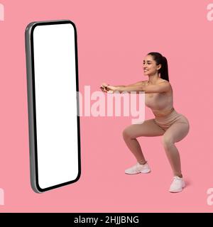 Woman Doing Deep Squats Near Big Phone On Pink Background Stock Photo