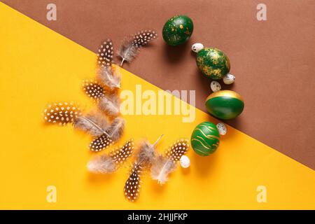 Frame made of stylish Easter eggs and feathers on color  background Stock Photo