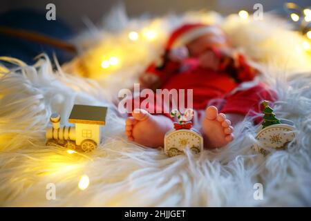 Baby feet on a fluffy blanket with toys, child in Santa costume. Selective focus, shallow depth of field. Stock Photo