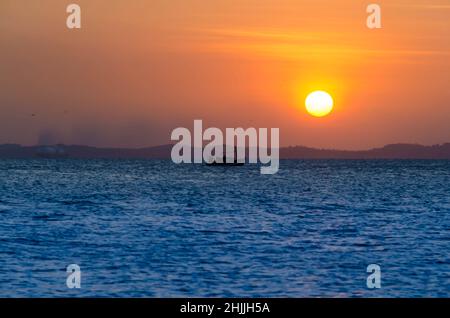 Sunset seen from Ribeira beach in Salvador, Bahia, Brazil. A boat sails at sea. Stock Photo