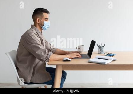 Man in protective facemask working on pc at home office Stock Photo