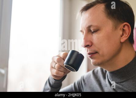 Portrait of Handsome young man drinking coffee espresso in the kitchen at home near the window Stock Photo