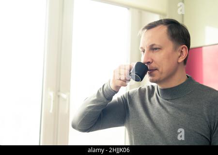 Portrait of Handsome young man drinking coffee espresso in the kitchen at home near the window Stock Photo